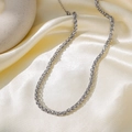 Close-up of silver stainless steel wheat chain necklace resting on soft yellow silk fabric - Steel / Necklace