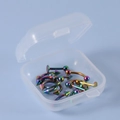 Makroansicht von 12 Regenbogen-Piercings aus Edelstahl in einer transparenten Box - bunt