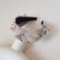 Elegante diadema beige con nudo y perlas decorativas sobre un maniquí blanco - Caqui