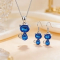 Detail view of blue cat-shaped crystal necklace and earrings set on beige silk fabric - Necklace + Earrings / Blue