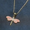 Close-up of golden dragonfly pendant necklace with pink enamel wings and white crystals - Pink