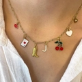 Detailed close-up of a gold charm necklace with enamel heart, cherry, and letter pendants - Style A