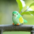 Miniature green resin bird figurine with yellow wings on a natural tree branch - Green Bird (Head Turned)