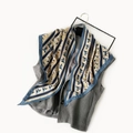 Detail of printed silk scarf with horse pattern draped on a grey vest against white background - Blue