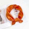 Detailed view of a bright orange satin scarf tied in a knot on a fashion magazine - Orange