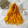 Bright yellow cashmere-like scarf with long tassels laid on white soft bedding - Yellow