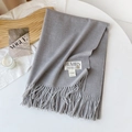 Detail of light grey cashmere-like scarf with fringe edges and brand label on a wooden tray - Gray