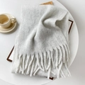 Dettaglio di una sciarpa grigia in mohair con nappe su un accogliente tavolo bianco - 40x210cm / grigio-bianco
