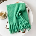 Primo piano di una morbida sciarpa in mohair verde menta con nappe su tavolo bianco - 40x210cm / Verde