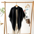 Detail of elegant black shawl with frayed edges hanging on a minimal wooden hanger - Black