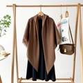 Detailed view of a brown tassel shawl on a wooden hanger paired with a black dress - Brown