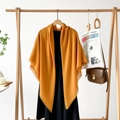 Close-up of ginger yellow tassel shawl on a wooden hanger with a black dress - Orange