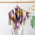 Detail view of abstract printed satin silk scarf styled as an accessory on a cream dress - Elegant Purple