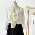Close-up of cream knitted shawl with logo patch paired with white shirt and black skirt - Milk Yellow
