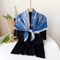 Close-up of blue and white printed silk scarf with feather pattern on a black top - Blue