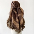 Detailed view of lightweight brown paisley scarf with gold patterns on a model's head - 90x90cm / Brown