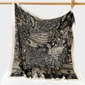 Detail eines Seidenschals mit Fischgrätmuster und Paisley-Print an einer Holzstange - Schwarz / 90x90cm