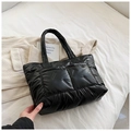 Detail of black quilted tote bag with padded down fabric and glossy texture on white linen - Black