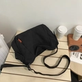 Minimalist black canvas messenger bag with orange woven label on a wooden desk - Black