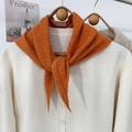 Dettaglio della sciarpa in maglia arancione con etichetta e cardigan beige su gancio in legno - Arancione