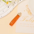 Macro detail of orange rhinestone leather keychain with golden metal clasp and woven texture - Orange