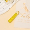 Macro detail of golden rectangular pendant with textured rhinestone inlay and tulip card - Gold