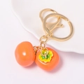 Porte-clés créatif en forme de kaki orange avec fermoir doré sur une assiette blanche - Style Kaki Orange