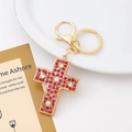 Macro detail of golden cross keychain with pink and red rhinestones on white tray - Cross Style 3