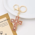 Detail of golden cross keychain with pink rhinestones on elegant white porcelain plate - Cross Style 1