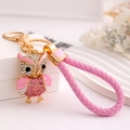 Détail du porte-clés chouette avec strass roses et lanière tressée sur support - Rose + Corde en Cuir