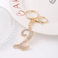 Detailed view of number 2 gold keychain with rhinestones and lobster clasp on ceramic plate - Number 2