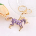 Dettaglio del portachiavi unicorno dorato con strass viola su una superficie bianca - Viola Scuro