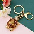Gros plan sur porte-clés tortue dorée avec strass marrons et fermoir mousqueton sur fond bicolore - Café