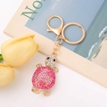 Goldener Schildkröten Schlüsselanhänger mit rosa Kristallen neben gelben Tulpen - Rosarot