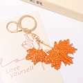 Detail eines Ahornblatt-Schlüsselanhängers mit orangefarbenen Steinen und Gold-Finish - Orangerot