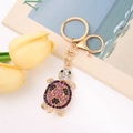 Détail d'un porte-clés tortue créatif orné de cristaux roses et noirs de style joaillerie - Violet