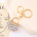 Primer plano detallado de un llavero de bolso dorado con pedrería brillante y patrones florales - Blanco