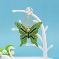 Dettaglio del portachiavi a farfalla con strass verdi e base dorata su un supporto - Verde