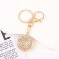 Close-up of golden rhinestone-encrusted round keyring with lobster clasp and metal chain - Letter O