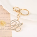 Close-up of golden letter H keychain with sparkling rhinestones on a white ceramic tray - Letter U(U) / Gold
