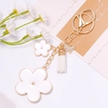 Close-up of golden butterfly keychain with white enamel flowers and leather tassel detail - White