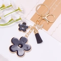 Detailed shot of golden keychain with black floral charms, rhinestone butterfly and tassel - Black