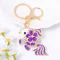 Detailed close-up of a golden fish keychain with purple gemstones and white crystals - Purple