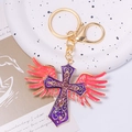 Golden cross keychain with purple rhinestones and pink wings on artistic tray - Cross Style 6