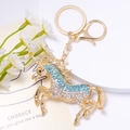 Vista macro di un portachiavi a forma di cavallo dorato con strass azzurri e bianchi - Stile Blu Bianco