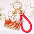 Detalle del llavero de corona dorada con strass rojos y correa de cuero trenzado - Corona Con Cuerda De Cuero Roja / Rojo