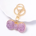 Dettaglio portachiavi a fiocco dorato con strass viola su un piatto bianco - Violetto