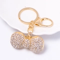 Macro di portachiavi a fiocco dorato con strass scintillanti su un piatto bianco - Bianco