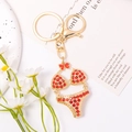 Golden bikini keychain with red rhinestones and lobster clasp on white floral background - Red