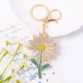 Macro detail of sunflower keychain with white, yellow and green rhinestones on gold alloy - White